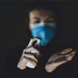 Eine Frau mit einem Mund-Nasen-Schutz desinfiziert ihre Hände.
