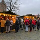 Menschen stehen vor drei Hütten auf dem Adventsmarkt Schloss Raesfeld.
