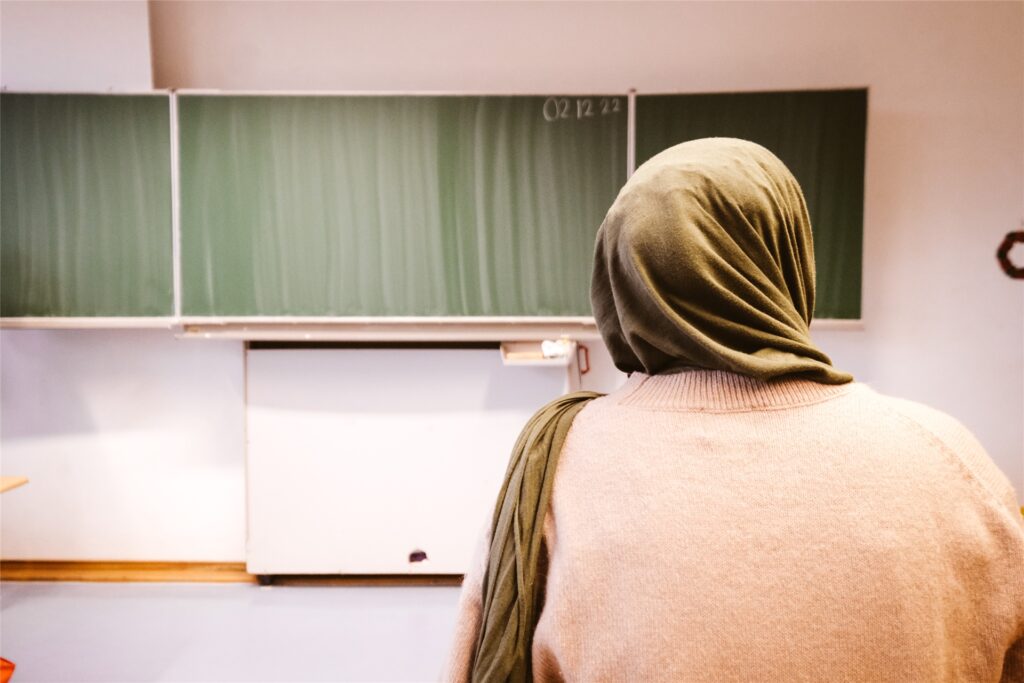 Eine junge Frau mit grünem Kopftuch sitzt vor einer Tafel. Eine junge Frau mit grünem Kopftuch sitzt vor einer Tafel.