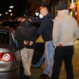 Ein Mann in Handschellen wird von zwei Polizisten in ein Auto gesetzt