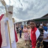 Der Nikolaus steht mit seinem Stab in der Hand auf dem Platz vor der Kita Am Wilhelmsplatz, neben ihm steht der vierjährige Miracle.