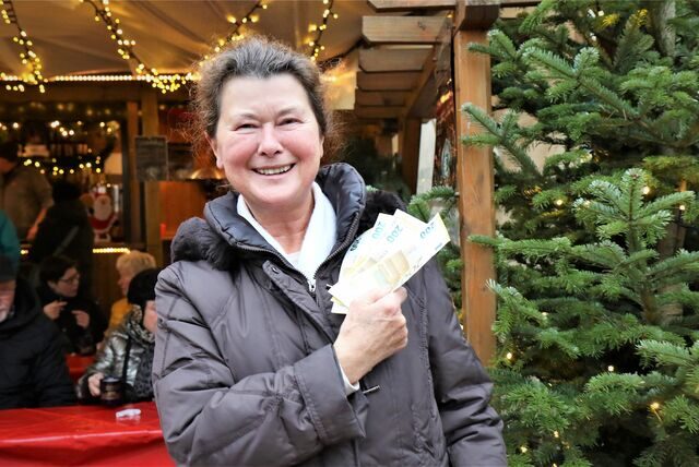 Eine Frau steht vor einer Weihnachtshütte und hält Geldscheine in der Hand