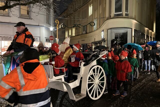 In einer weißen Kutsche sitzt in Recklinghausen ein als Nikolaus verkleideter Mann neben zwei als Wichtel verkleideten Kindern. Hinter der Kutsche warten weitere Wichtel und einige Eltern.