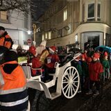 In einer weißen Kutsche sitzt in Recklinghausen ein als Nikolaus verkleideter Mann neben zwei als Wichtel verkleideten Kindern. Hinter der Kutsche warten weitere Wichtel und einige Eltern.