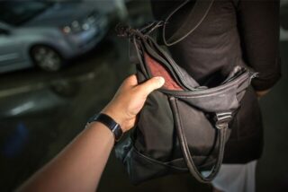 Eine Männerhand greift im Dunkeln nach einer Handtasche, die über der Schulter einer Frau hängt (Symbolbild)