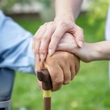 junge hände liegen auf einer älteren hand die einen gehstock hält