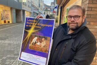 Kai Dörnhoff steht auf der Großen Geldstraße in Recklinghausen und hält ein Plakat des Hochlarer Krippenspiels in Händen.