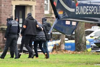 Eine Person (2.v.r.) wird von Polizisten aus einem Hubschrauber gebracht.