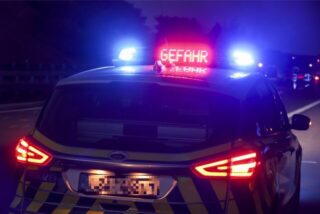Ein Polizeiauto bei Dunkelheit warnt mit „Gefahr“-Anzeige.