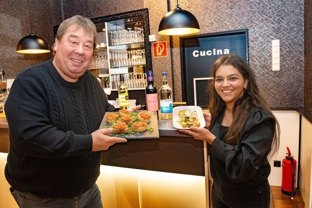 Detlef „Didi“ Pourie und Aleyna Akpinar freuen sich auf das Benefizessen zugunsten der Obdachlosen in Dortmund. Sie zeigen die Vorspeise, die serviert wird. Im Hintergrund ein Rotwein und eine Flasche Wasser.