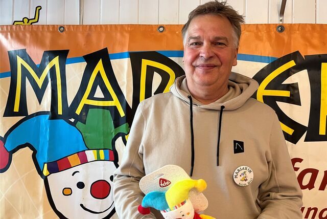 Uli Häring steht mit der Marlekin-Puppe vor einem Marlekin-Banner.