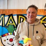 Uli Häring steht mit der Marlekin-Puppe vor einem Marlekin-Banner.
