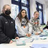 Die Schülerinnen Josefine, Eileen und Lykka von der Gesamtschule Waltrop haben Geschirrhandtücher und Plastikboxen vor sich liegen.