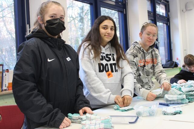 Die Schülerinnen Josefine, Eileen und Lykka von der Gesamtschule Waltrop haben Geschirrhandtücher und Plastikboxen vor sich liegen.
