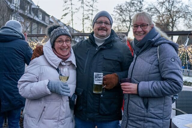 Zwei Frauen und ein Mann stehen in winterlicher Kleidung mit Gläsern in der Hand vor der Kamera.