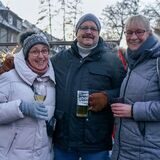 Zwei Frauen und ein Mann stehen in winterlicher Kleidung mit Gläsern in der Hand vor der Kamera.