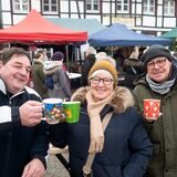 Zwei Männer und eine Frau stoßen mit Glühwein an, im Hintergrund ein Fachwerkhaus.
