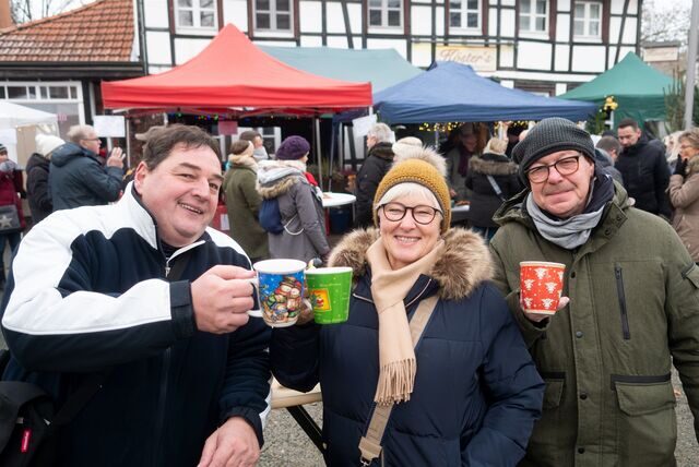 Zwei Männer und eine Frau stoßen mit Glühwein an, im Hintergrund ein Fachwerkhaus.