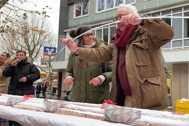 Rechtsanwalt Andreas Hebestreit und Kathrin Wolf vom Haus der Kulturen stehen mit einem Zollstock hinter einem riesigen Christstollen in der Hertener Fußgängerzone.