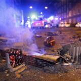 Abgebrannte Böller liegen nach der Silvesternacht auf der Straße, während im Hintergrund Einsatzkräfte der Feuerwehr stehen.
