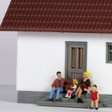 Symbolbild zur Grundsteuer-Erhöhung: Kunststoff-Figuren, die  eine Familie darstellen, sitzen vor dem Modell eines Wohnhauses.