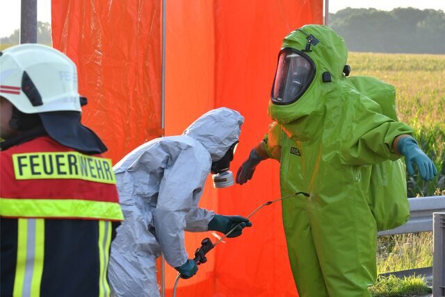Feuerwehrleute in Schutzanzügen werden nach einem Einsatz mit einer großen Menge Salpetersäure dekontaminiert.