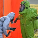 Feuerwehrleute in Schutzanzügen werden nach einem Einsatz mit einer großen Menge Salpetersäure dekontaminiert.