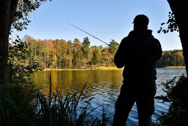 Ein Angler versucht mit einer Spinnangel an einem See einen Fisch zu fangen.