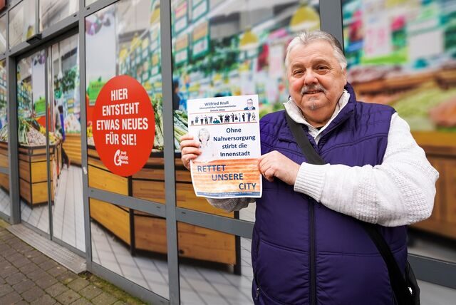 Wilfried Krull zeigt einen seiner Flyer „Rettet unsere City“ vor dem ehemaligen Rewe-Markt in der Stadtgalerie.