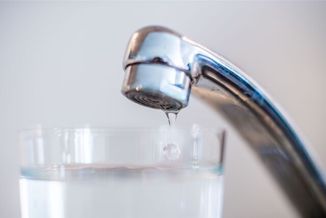 Aus einem Wasserhahn tropft Wasser in ein darunter stehendes Glas. (Symbolbild)