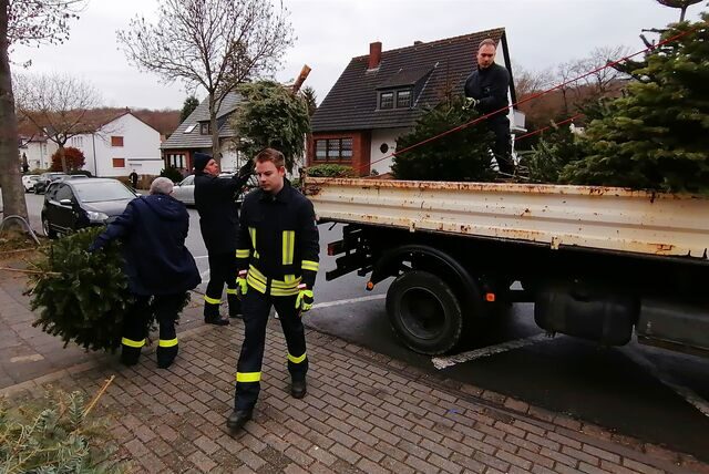 Vier Feuerwehrleute packen Tannenbäume auf die offene Ladefläche eines Lastwagens.
