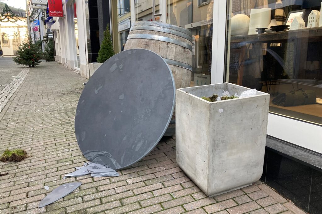 An einem stehenden Holzfass an der Große Geldstraße in Recklinghausen lehnt eine runde Schieferplatte, von der Teile abgebrochen sind.