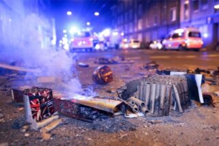 Abgebrannte Böller liegen nach der Silvesternacht auf der Reisholzer Straße, während im Hintergrund Einsatzkräfte der Feuerwehr stehen.