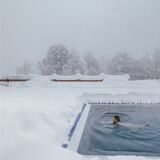 frau schwimmt im pool währenddessen um sie herum überall schnee zu sehen ist