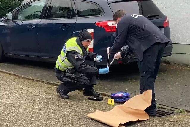 Ein Polizist und ein Kriminaltechniker sichern in einer Einfahrt an der Straße über den Knöchel in Herten einen Kinderrucksack und eine Mütze als Beweismittel.