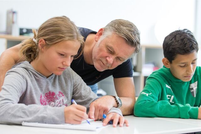 Ein Lehrer an einer weiterführenden Schule hilft einer Schülerin beim Bearbeiten einer Aufgabe.
