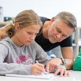 Ein Lehrer an einer weiterführenden Schule hilft einer Schülerin beim Bearbeiten einer Aufgabe.