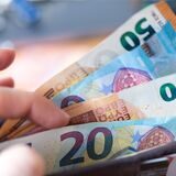Eine Frau hält ein Portemonnaie in der Hand, in dem Geldscheine stecken.