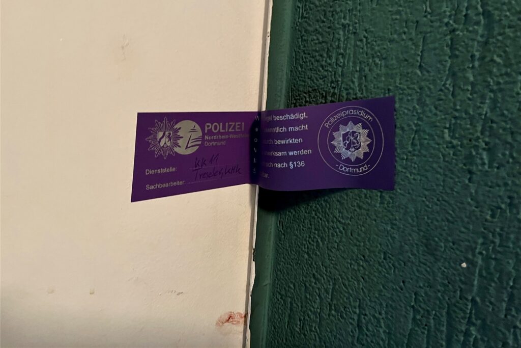 An der Wohnungstür des Opfers klebt am Samstag (14.1.) ein Siegel der Polizei Dortmund über einem verschmierten Blutfleck. Der Mann wurde in seiner Wohnung mit einem Messer angegriffen.