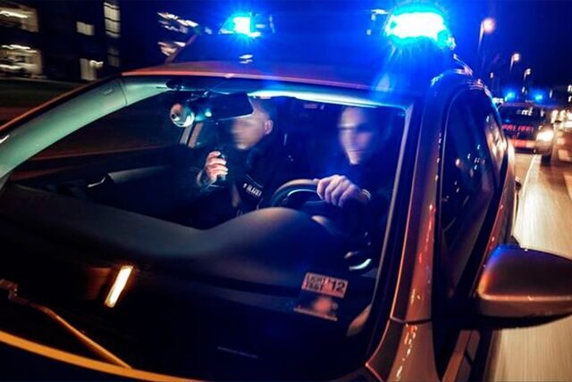Zwei Polizeibeamte sitzen im Streifenwagen mit Blaulicht.