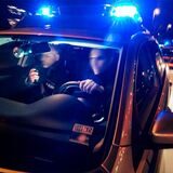 Zwei Polizeibeamte sitzen im Streifenwagen mit Blaulicht.