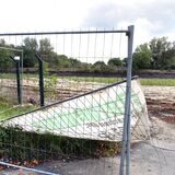 Ein abgrissenes Baustellenschild liegt hinter einem Bauzaun.