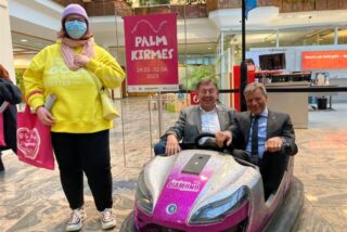Christoph Tesche, Bürgermeister von Recklinghausen, und Richard Abendroth, Vorsitzender des Schaustellervereins Recklinghausen, sitzen im Foyer der Sparkasse in einem Autoscooter. Links daneben steht eine junge Frau.