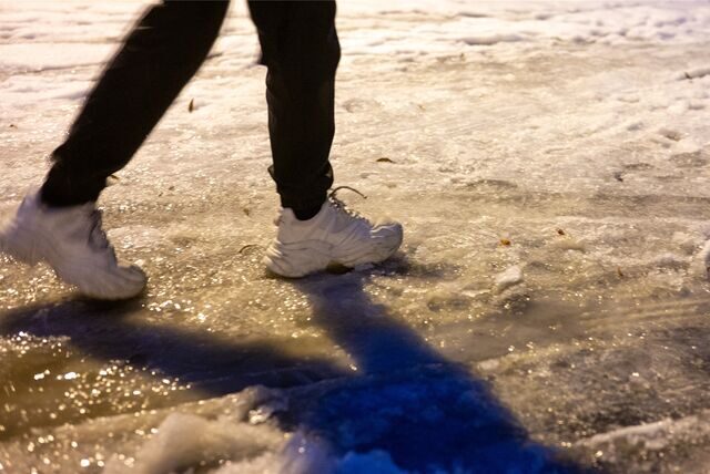Eine Fußgängerin ist am frühen Morgen auf einer Straße, die mit einer dünnen Eisschicht überzogen ist unterwegs. (Symbolbild)