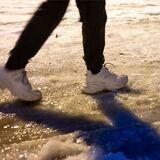 Eine Fußgängerin ist am frühen Morgen auf einer Straße, die mit einer dünnen Eisschicht überzogen ist unterwegs. (Symbolbild)