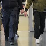 Eine Person ist mit Handschellen an einen Justiz-Mitarbeiter gekettet.