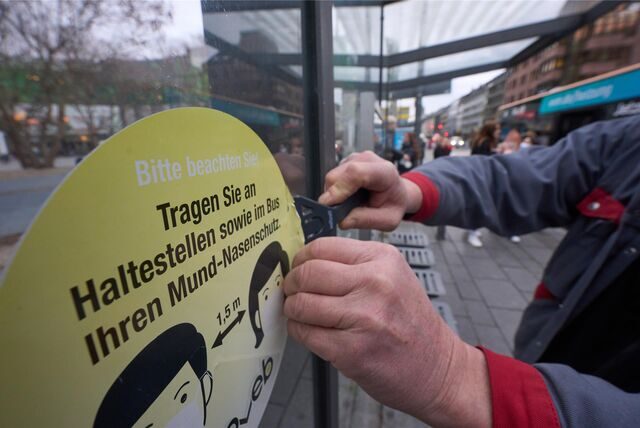 Ein Mitarbeiter der Koblenzer Verkehrsbetriebe entfernt an einer Haltestelle einen Aufkleber, der die Fahrgäste zum Tragen von Masken auffordert.