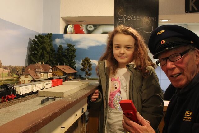 Die kleine Zoey Klahsen steht neben Arnold Eickenscheidt, der eine Lokführer-Uniform trägt. Er bedient eine Modelleisenbahn.