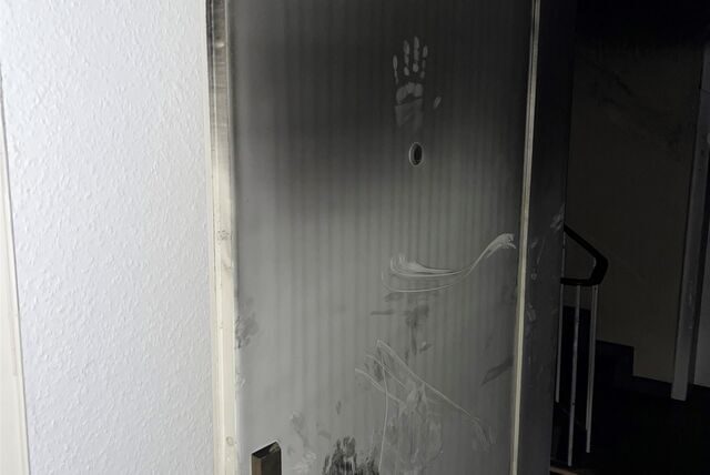 Wohnungstür mit Ruß bedeckt. Ein Handabdruck eines Feuerwehrmanns ist oberhalb des Spions zu erkennen.