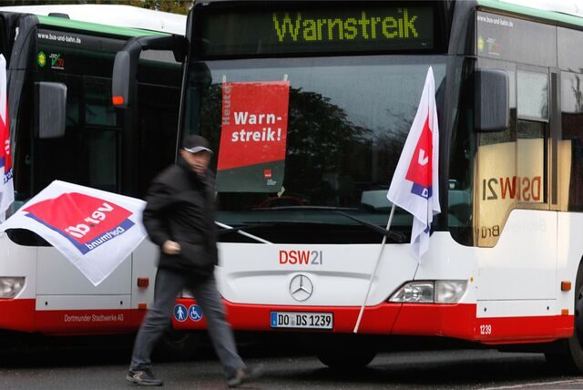 Ein streikender Busfahrer läuft mit einer Flagge der Gewerkschaft Verdi an einem Bus vorbei.